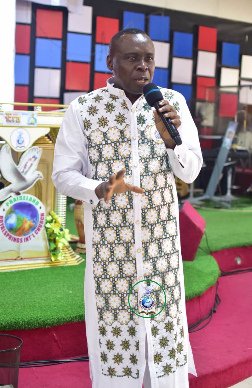 Apostle Prof. E. C. Ejiofor preaching with a microphone, wearing a white robe with gold and green star embroidery